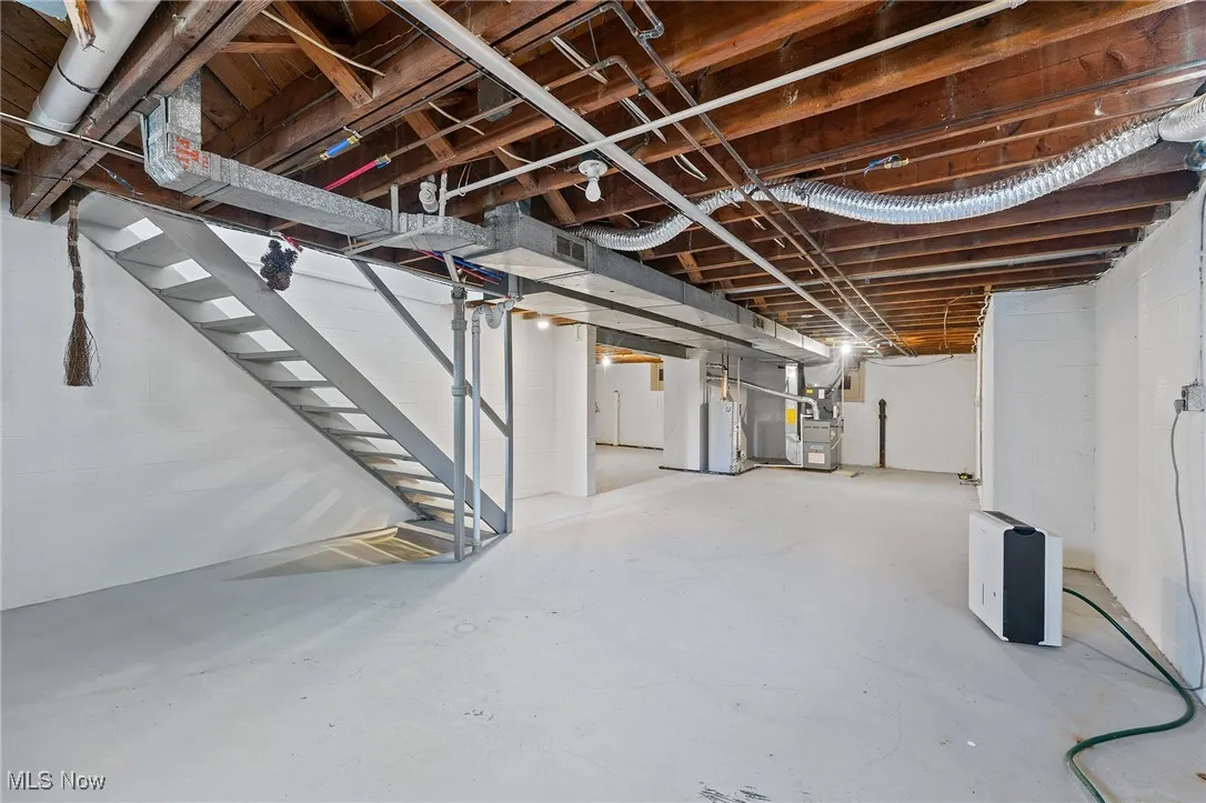 Unfinished basement with gas water heater, heating unit, and stairs