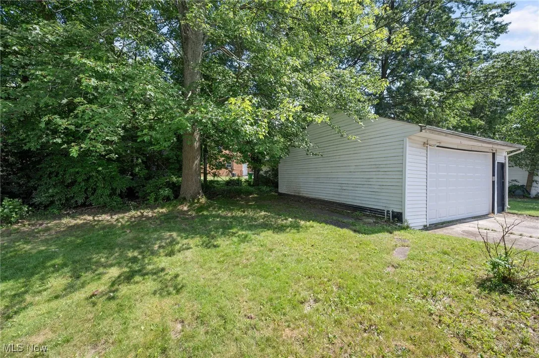 View of grassy yard with a detached garage and concrete driveway
