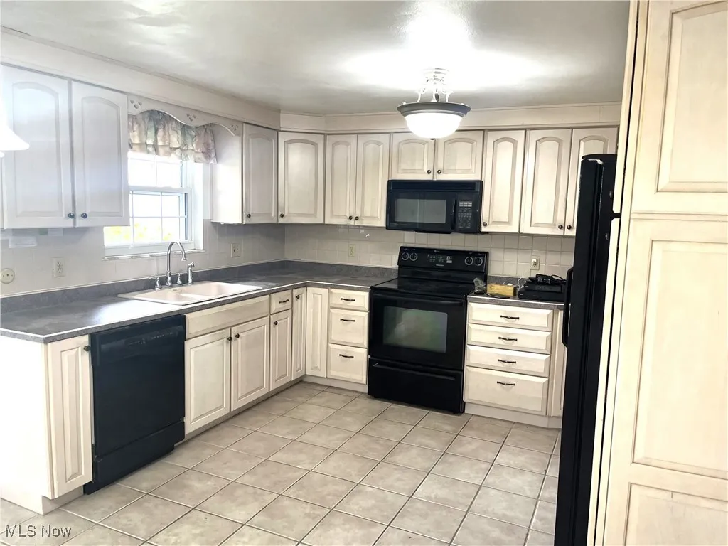Kitchen with black appliances, decorative backsplash, light tile patterned flooring, and dark countertops
