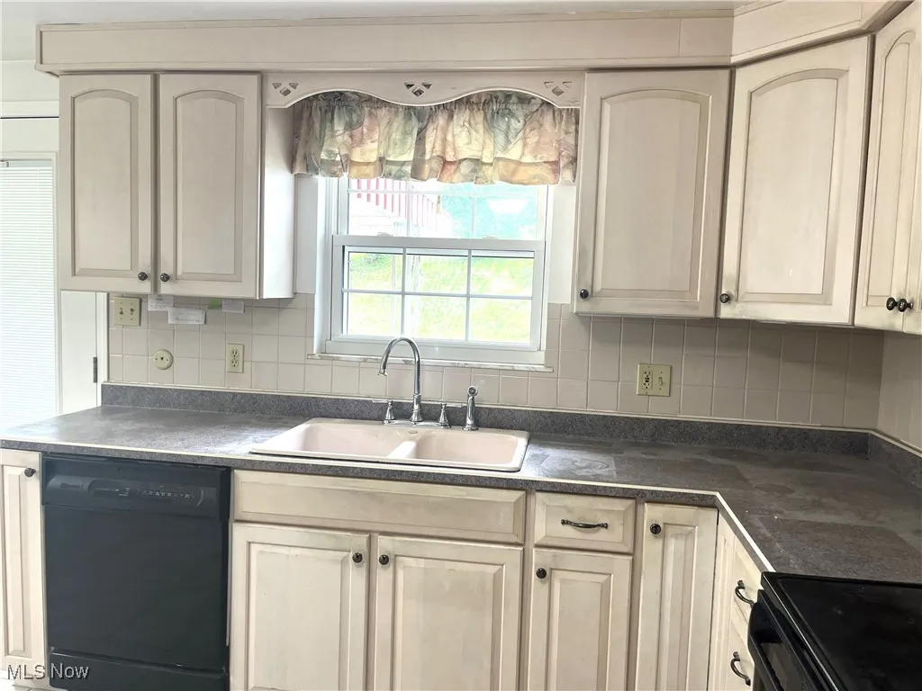 Kitchen featuring black appliances, tasteful backsplash, dark countertops, and cream cabinets