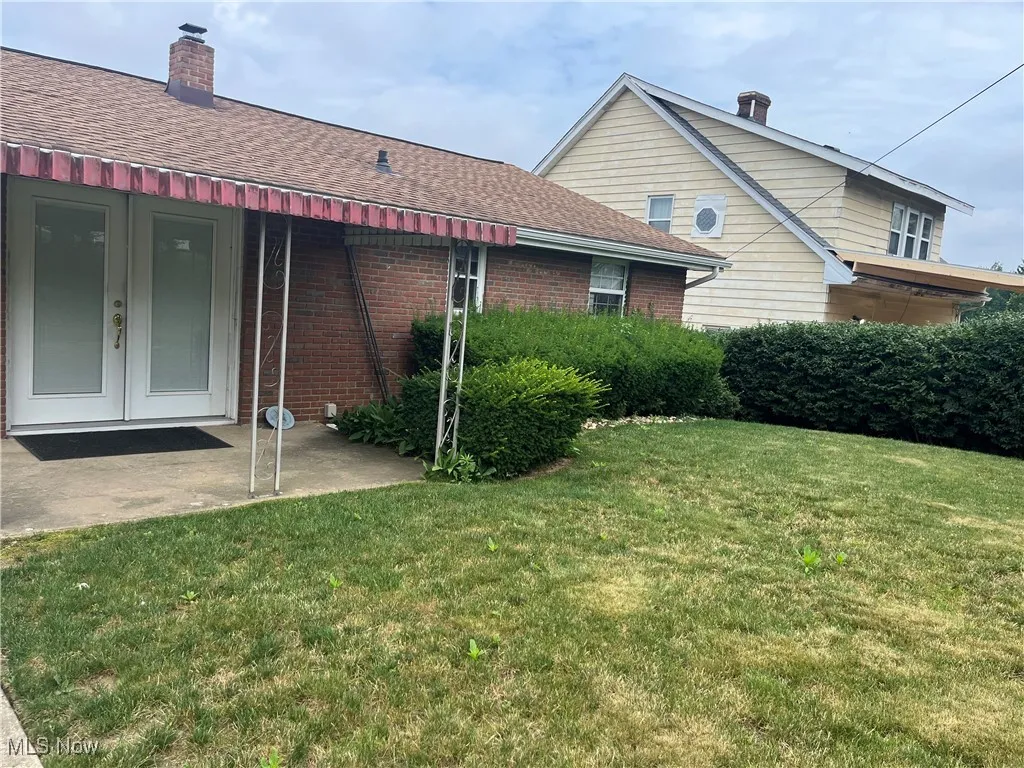 Back of house featuring french doors, a lawn, a chimney, brick siding, and a shingled roof