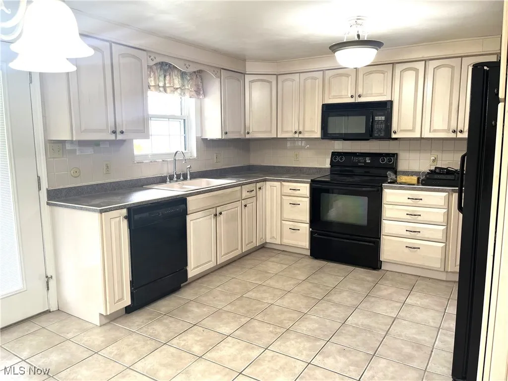 Kitchen with black appliances, tasteful backsplash, light tile patterned floors, and dark countertops