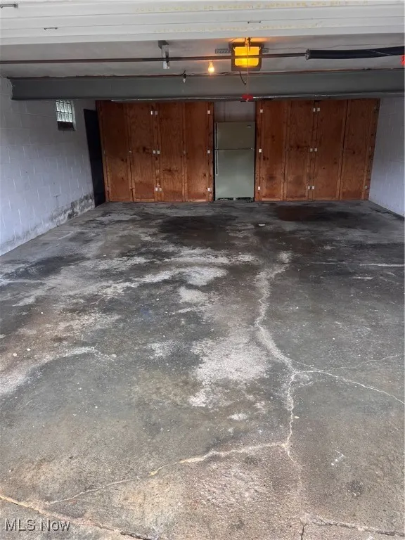Garage with concrete block wall, refrigerator, and a garage door opener