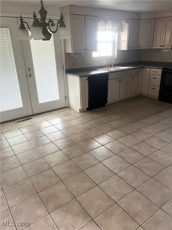 Kitchen featuring black appliances, light tile patterned floors, a chandelier, dark countertops, and french doors