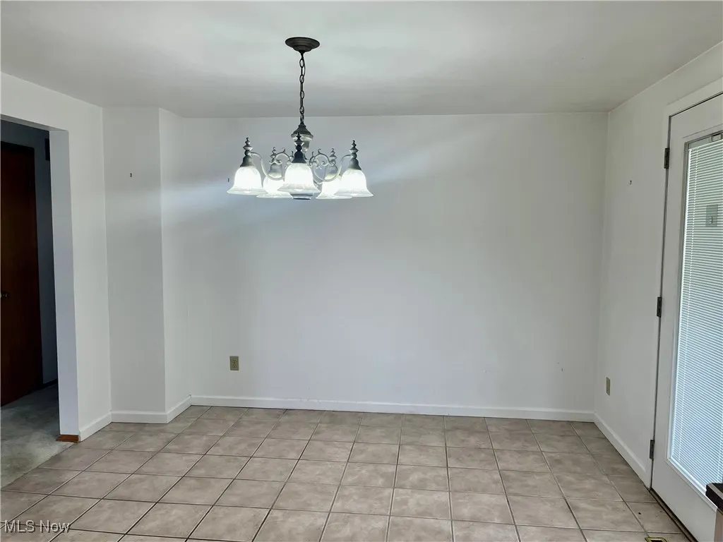 Unfurnished room featuring a chandelier and baseboards