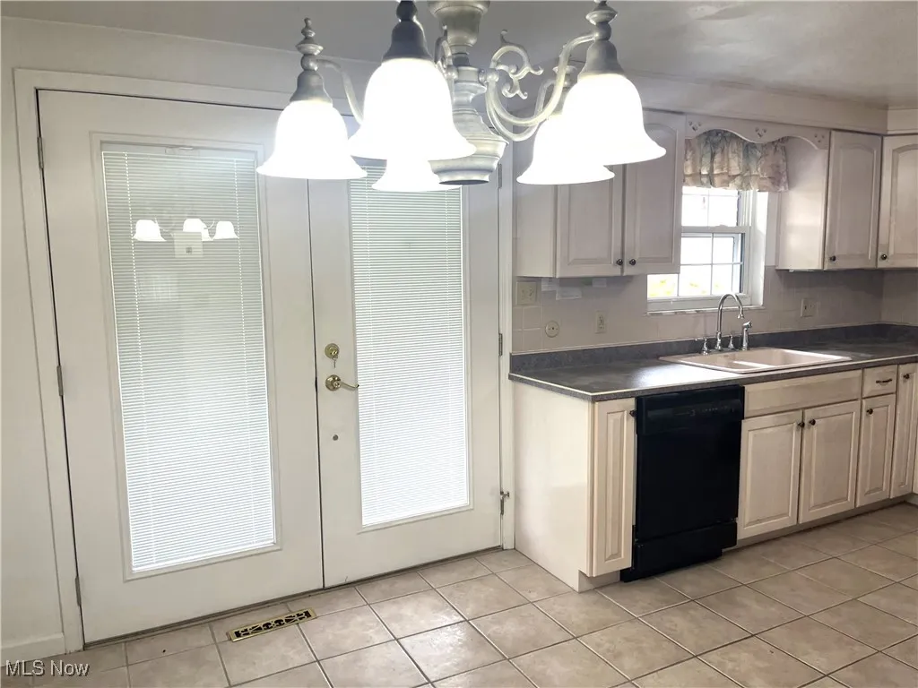 Kitchen with black dishwasher, dark countertops, light tile patterned floors, and decorative backsplash