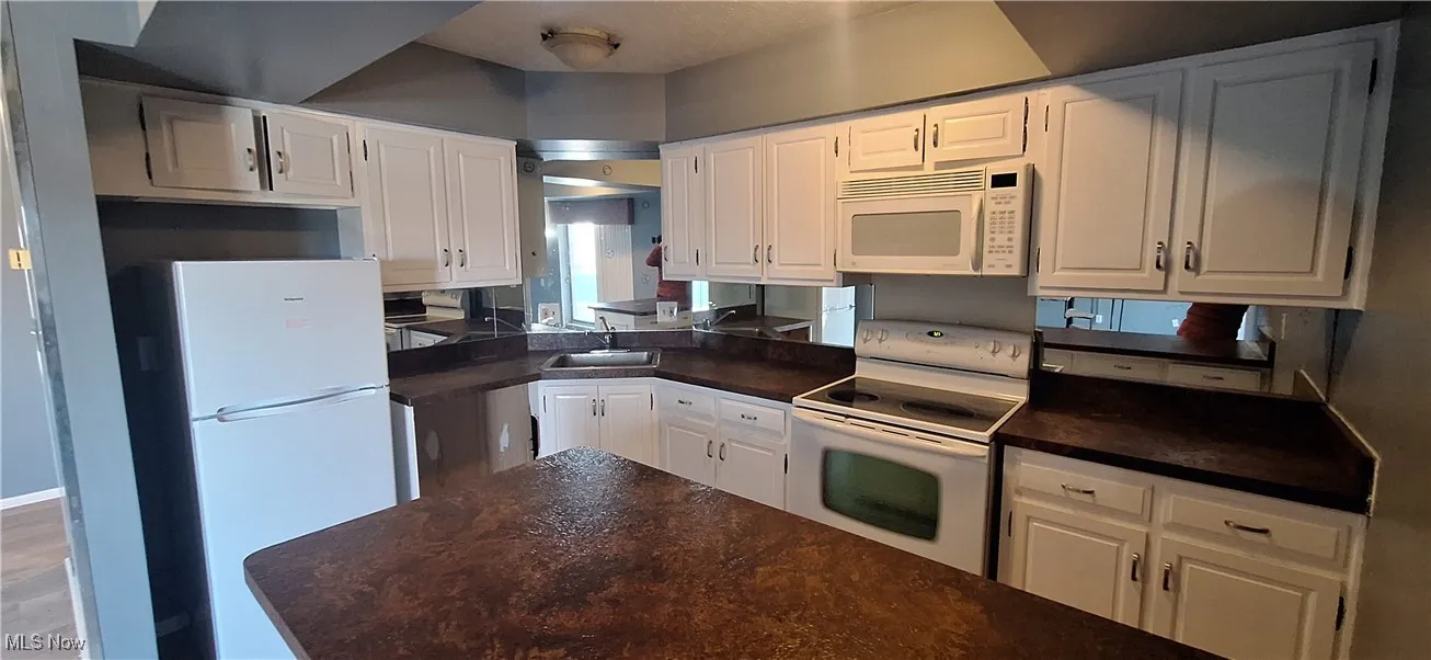 Kitchen with white appliances, dark countertops, and white cabinetry