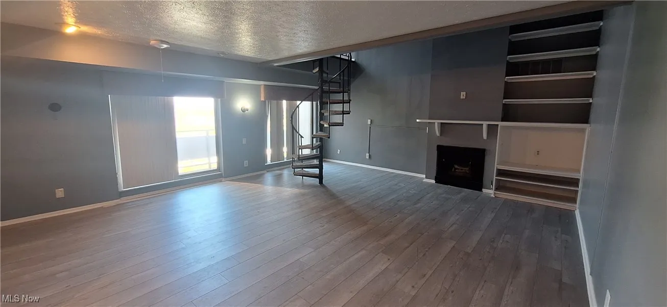 Unfurnished living room with stairway, a textured ceiling, wood finished floors, and a fireplace