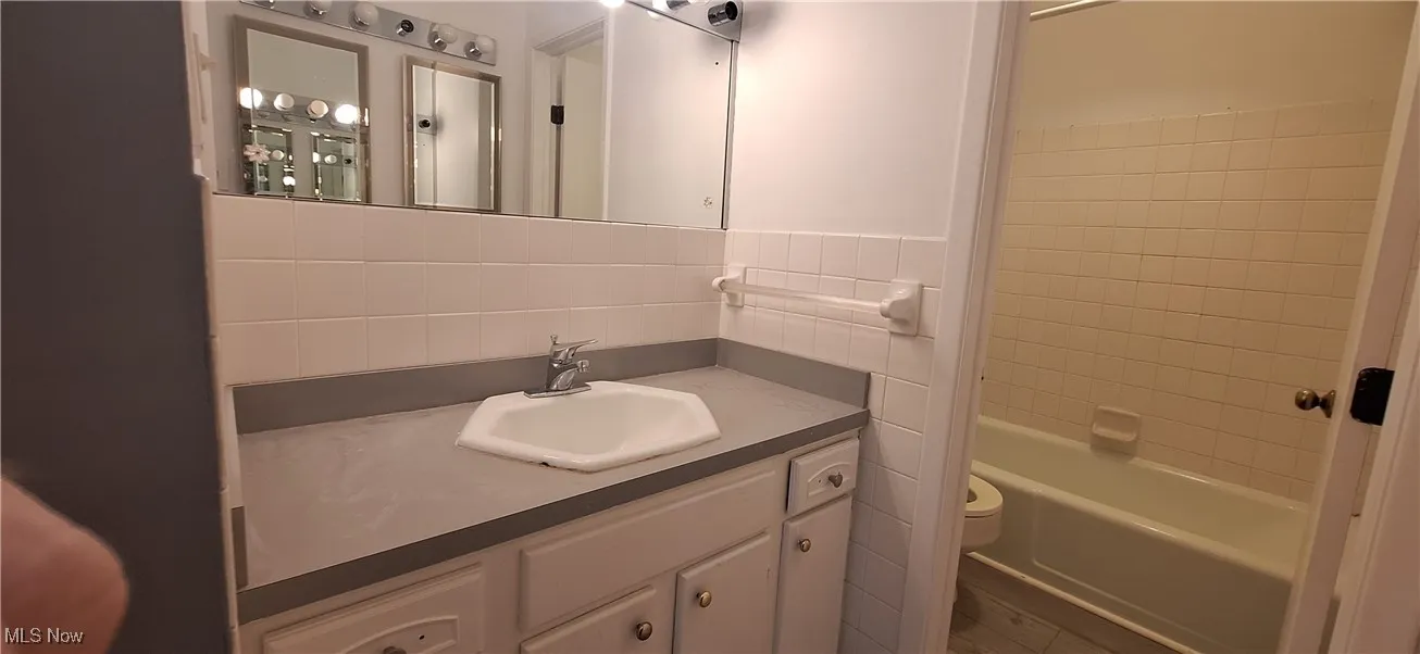 Bathroom featuring vanity, tile walls, and bathtub / shower combination
