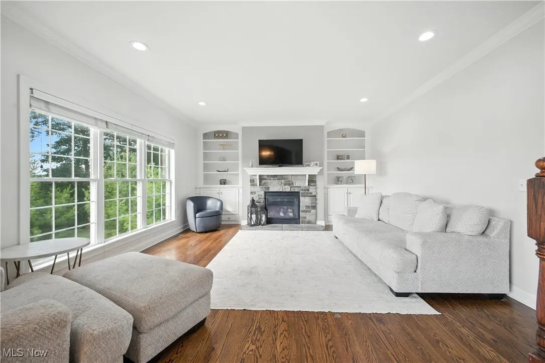 Living room featuring crown molding, wood finished floors, a fireplace, recessed lighting, and built in features