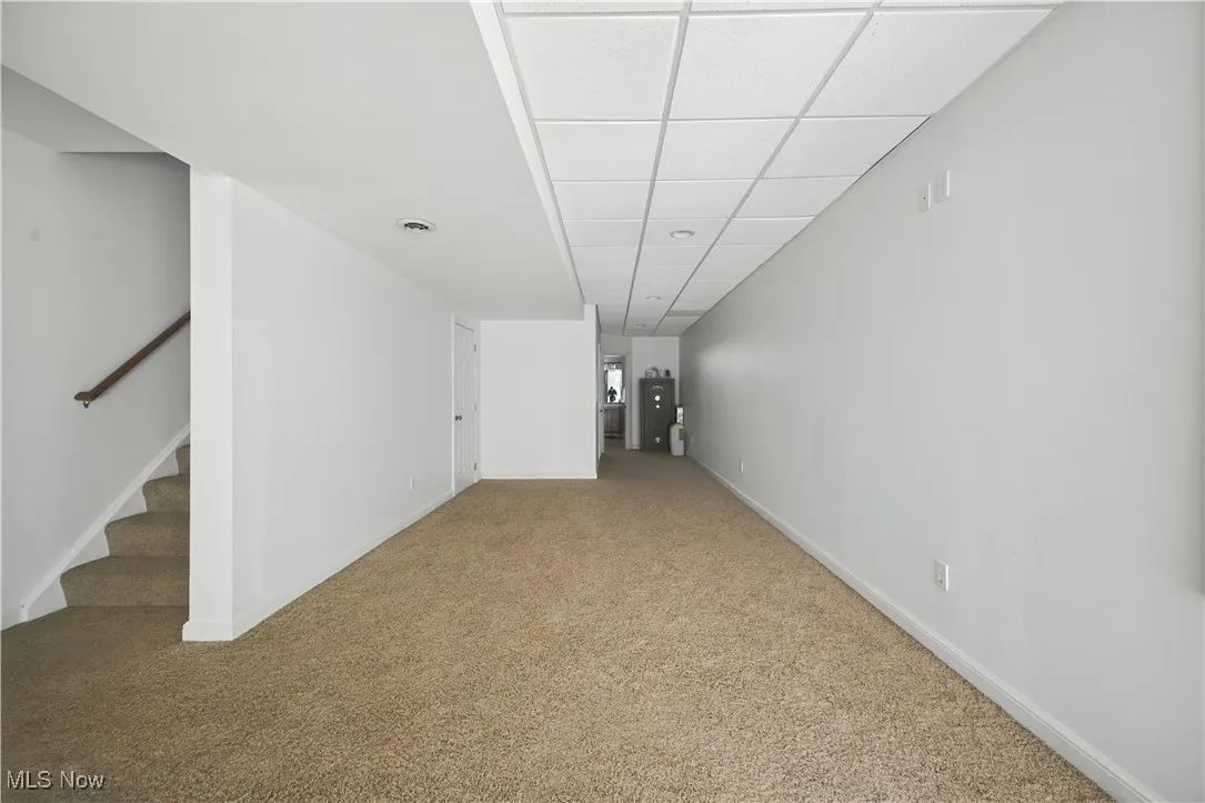 Below grade area featuring carpet flooring, stairway, and a drop ceiling