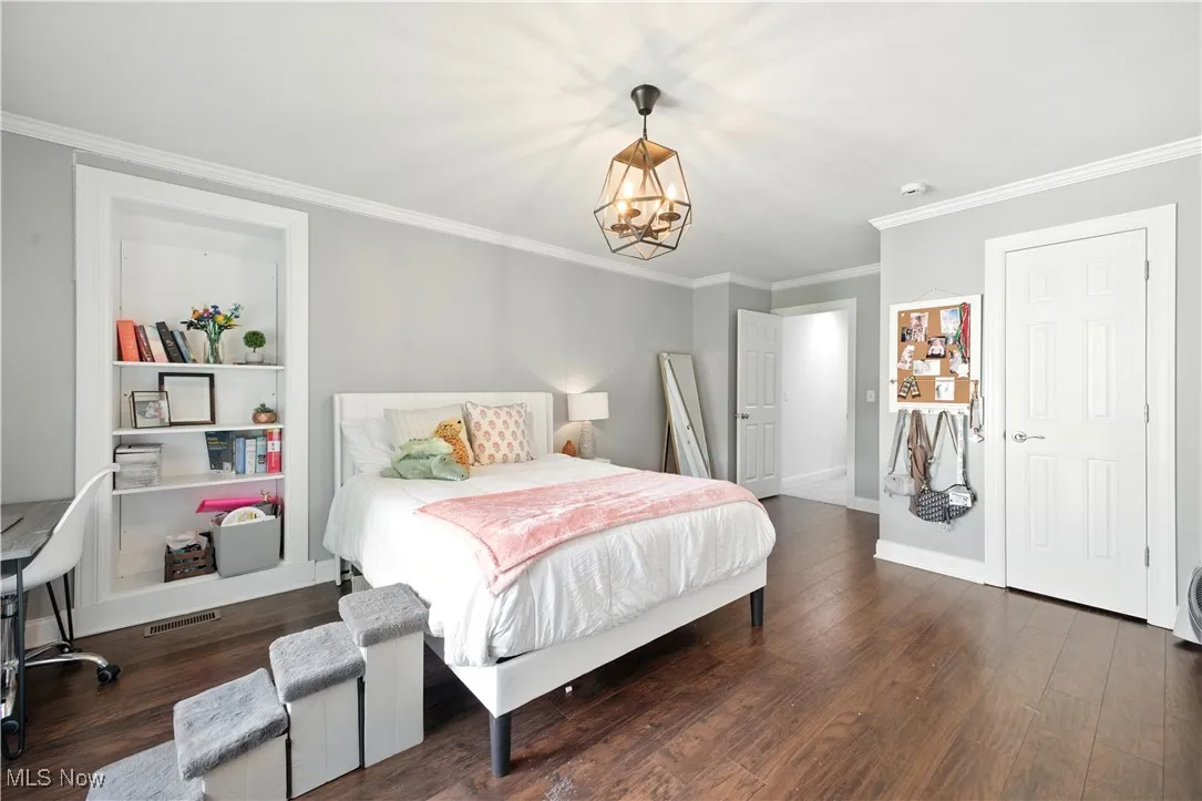 Bedroom with a chandelier, ornamental molding, and wood finished floors with storage behind built ins.