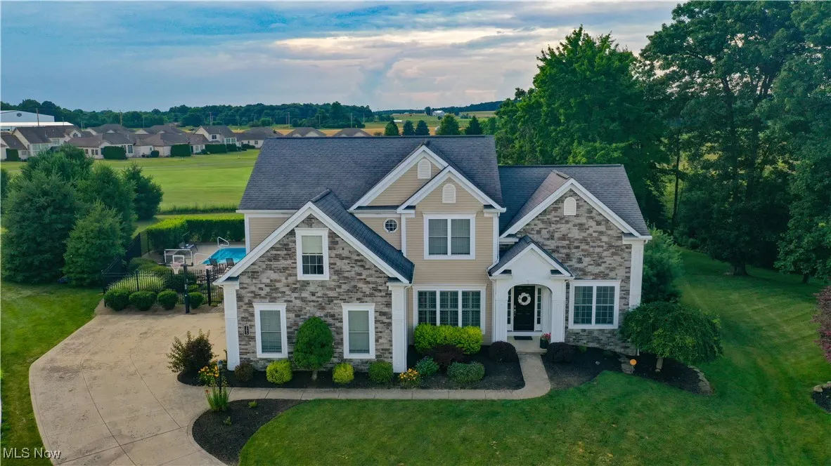 Traditional-style home featuring stone siding, driveway, and a front lawn