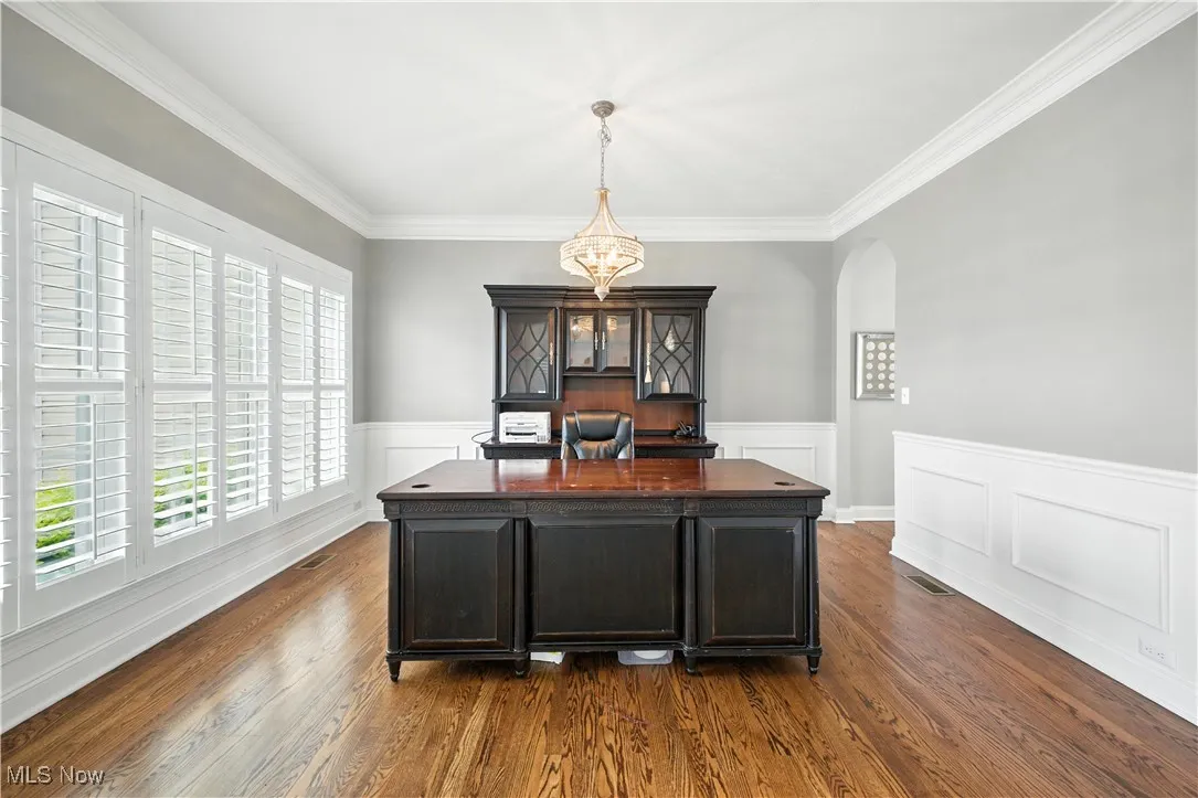 Formal dining room currently being used as an office area featuring arched walkways, dark wood-type flooring, crown molding, and wainscoting