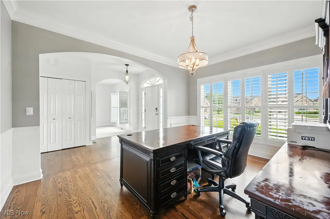Formal dining room currently being used as a home office featuring arched walkways, wood finished floors, crown molding, a chandelier, and wainscoting