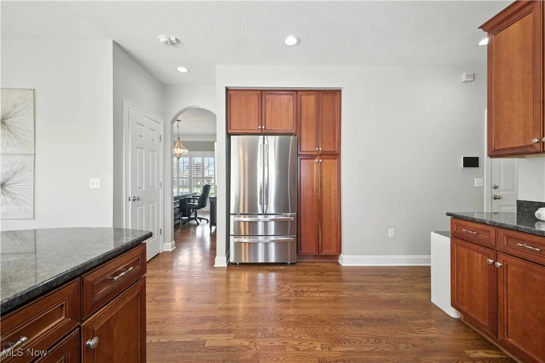 Kitchen featuring freestanding refrigerator, dark wood-style floors, arched walkways, dark stone countertops, and recessed lighting