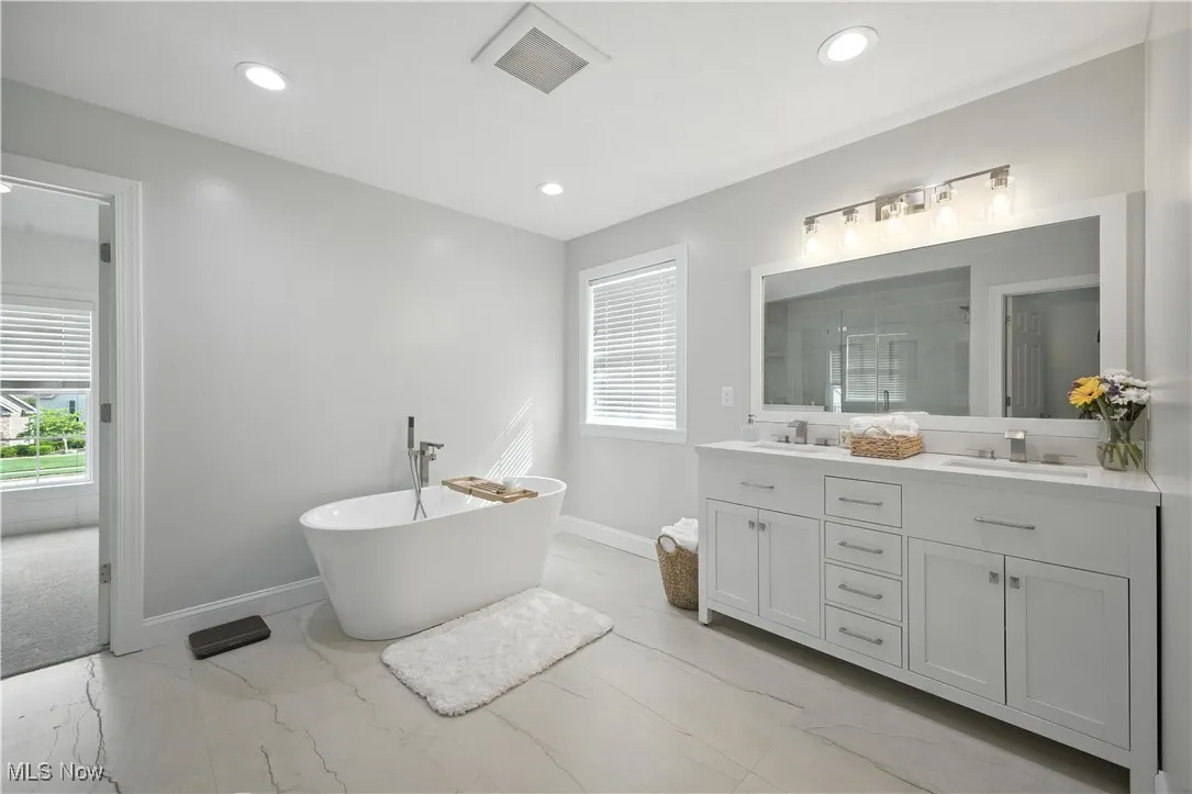 Full bath featuring double vanity, marble finish flooring, a soaking tub, a shower stall, and healthy amount of natural light