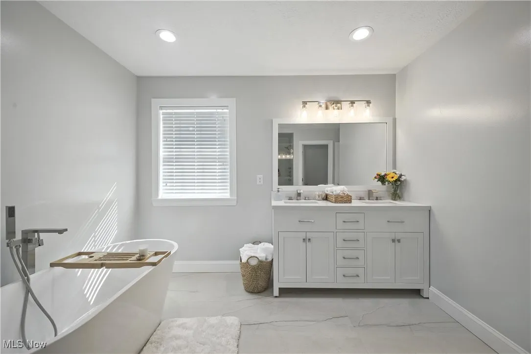 Full bath featuring double vanity, a freestanding bath, marble look tiles, and recessed lighting