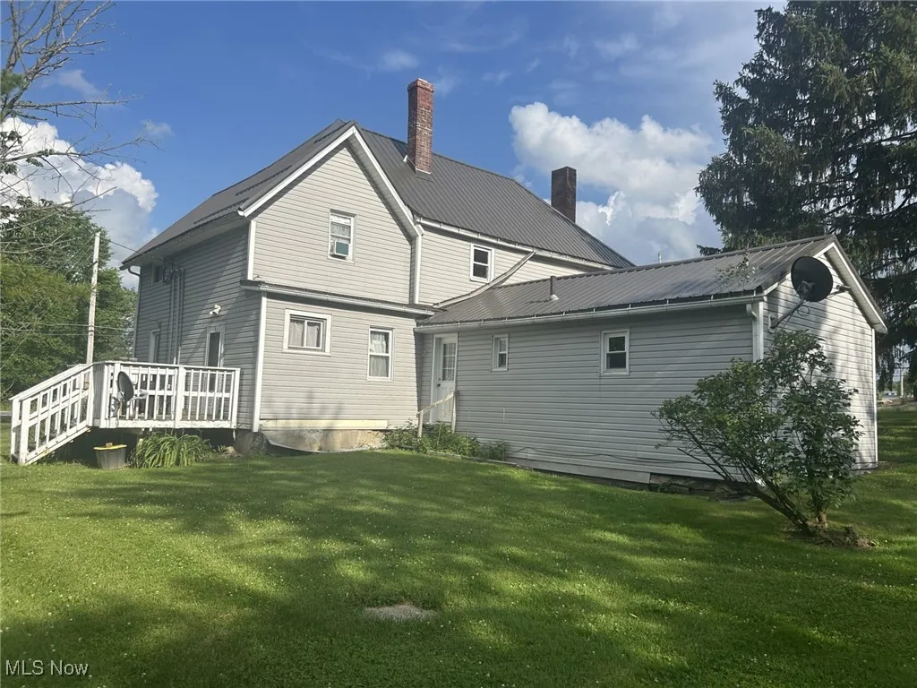 Back of house featuring a chimney, a lawn, a wooden deck, and a metal roof