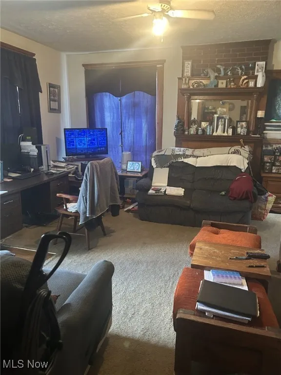 Living room with carpet floors, a desk, a ceiling fan, and a textured ceiling