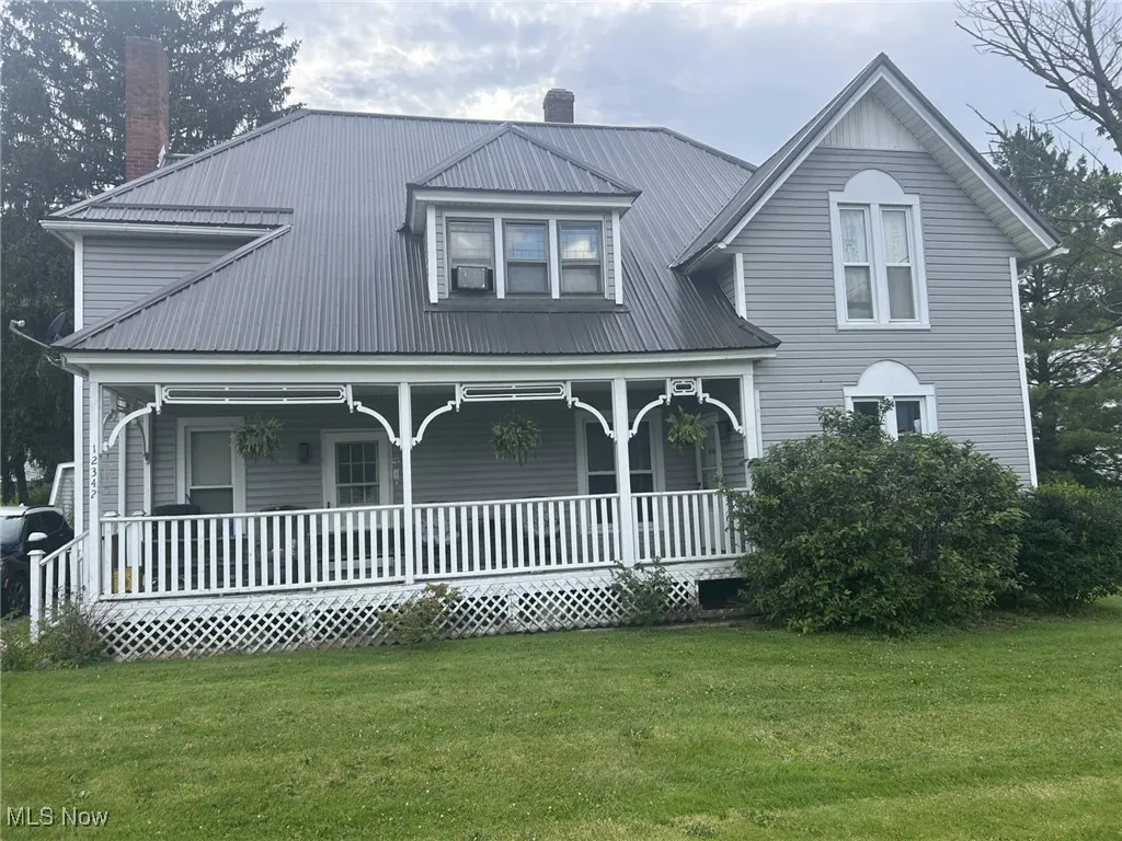 View of front of house featuring a chimney, covered porch, a front lawn, and a metal roof