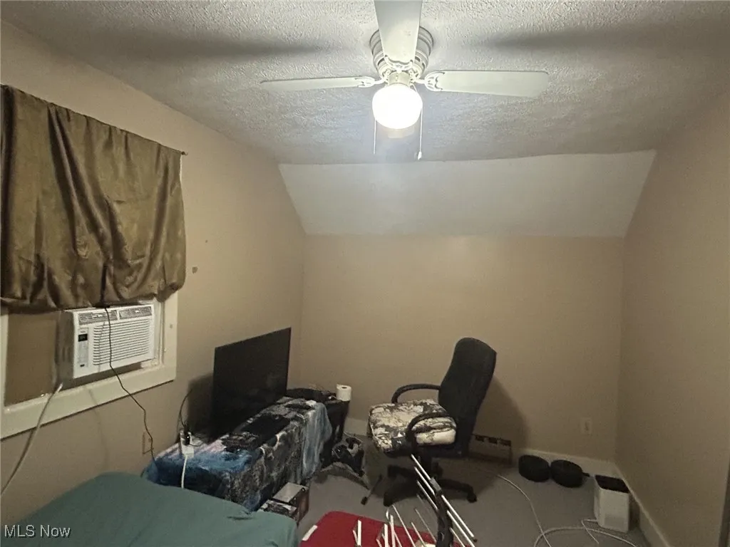 Bedroom with a textured ceiling, vaulted ceiling, ceiling fan, cooling unit, and carpet flooring