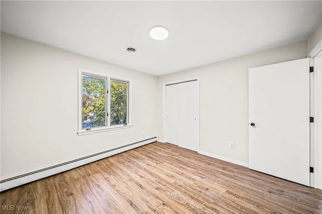 Unfurnished bedroom featuring a closet, light hardwood / wood-style flooring, and a baseboard heating unit