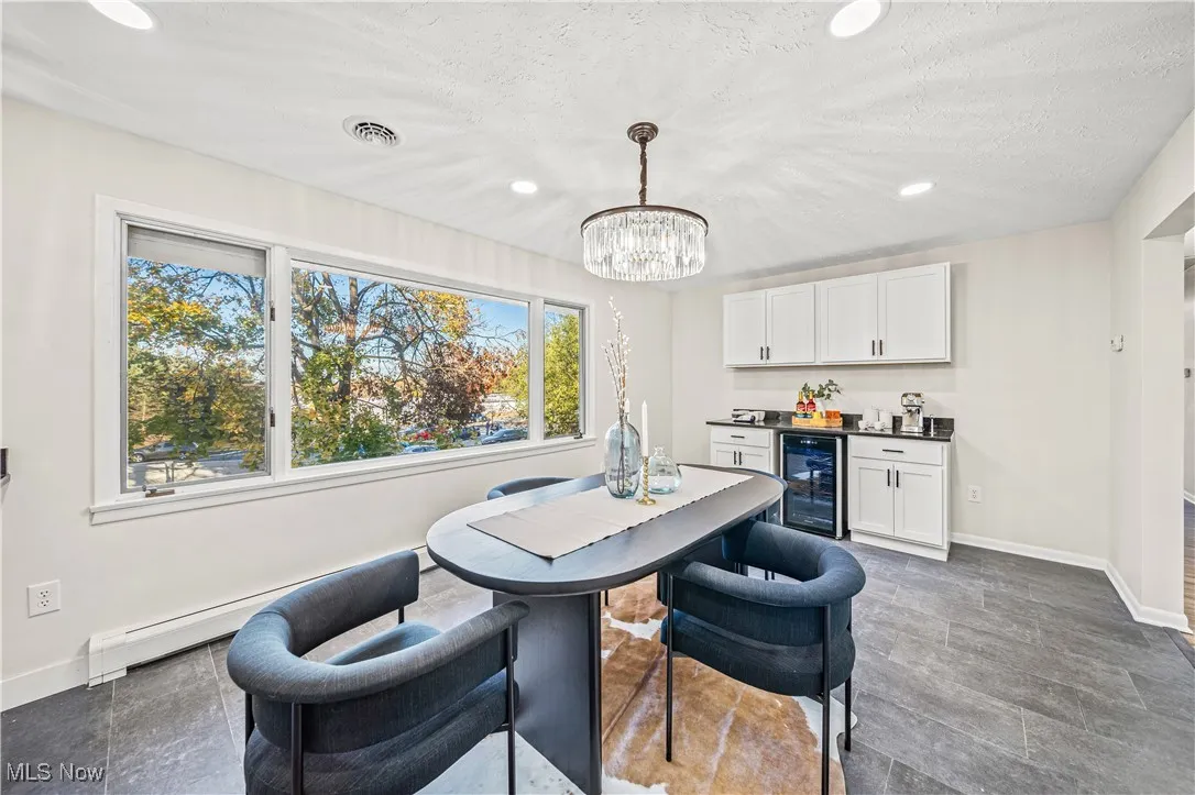 Dining room featuring a baseboard radiator, wine cooler, a notable chandelier, a textured ceiling, and indoor bar