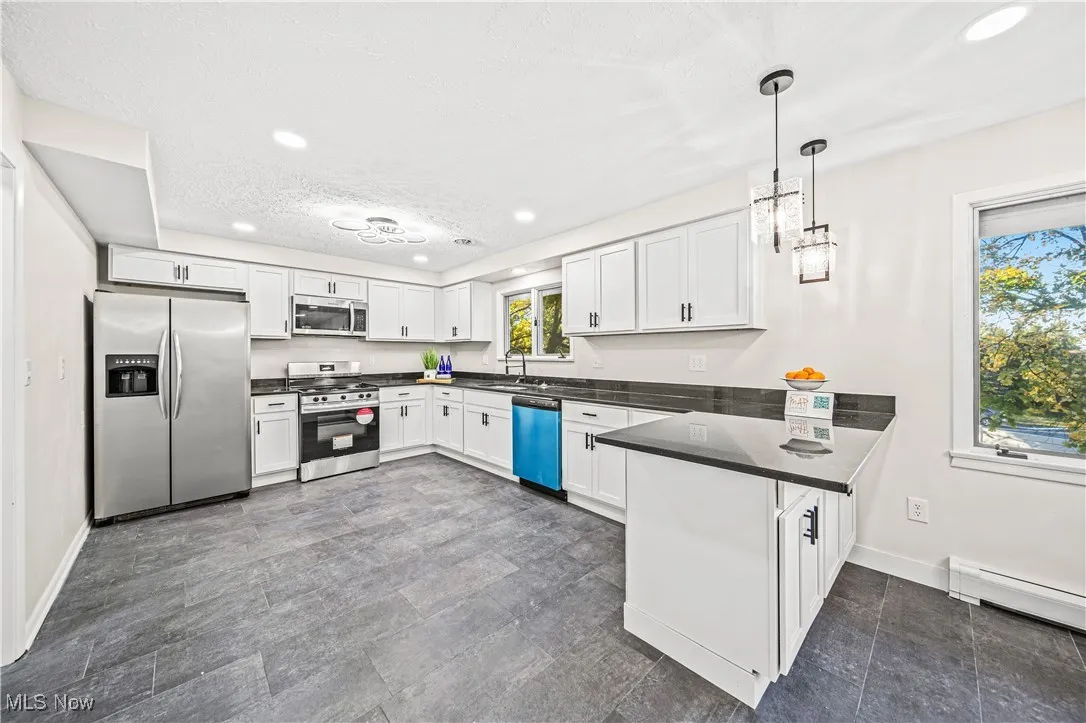 Kitchen featuring kitchen peninsula, white cabinets, appliances with stainless steel finishes, and pendant lighting
