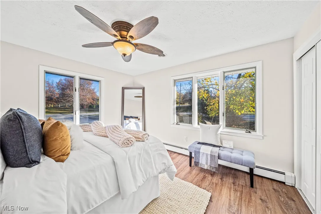 Bedroom featuring a closet, a textured ceiling, a baseboard radiator, ceiling fan, and wood-type flooring