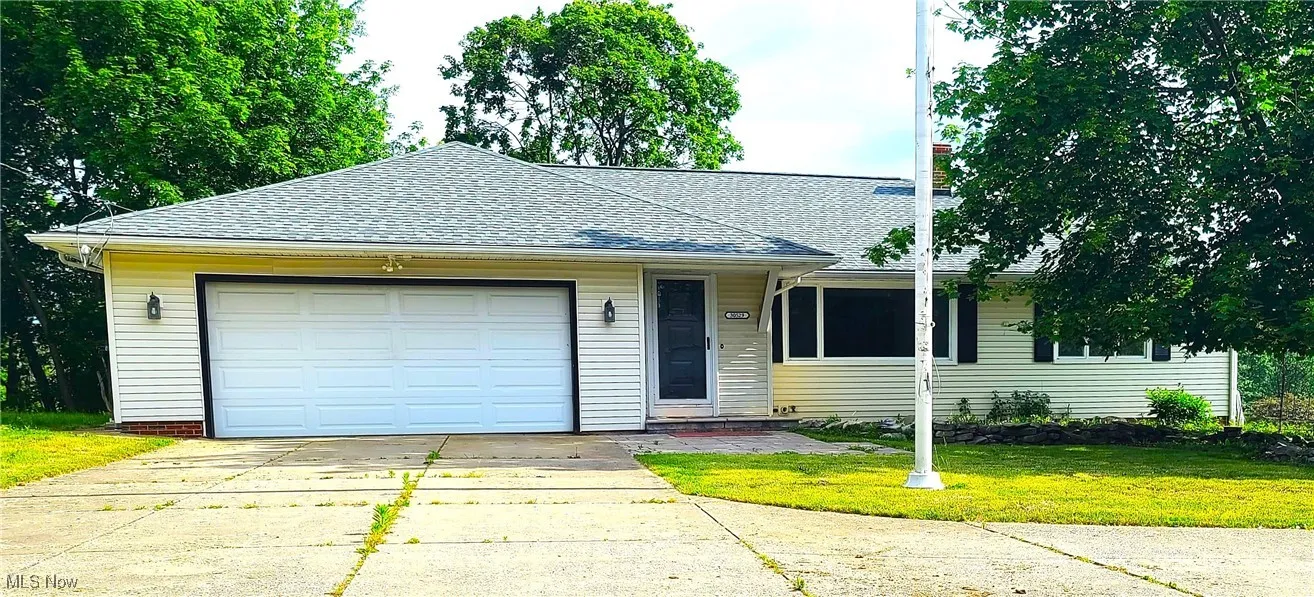 View of front of house featuring roof with shingles, driveway, a front yard, and an attached garage