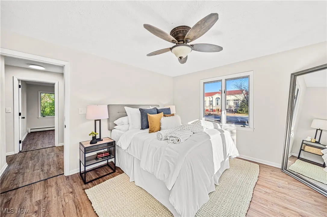 Bedroom featuring a baseboard radiator, ceiling fan, multiple windows, and light hardwood / wood-style floors