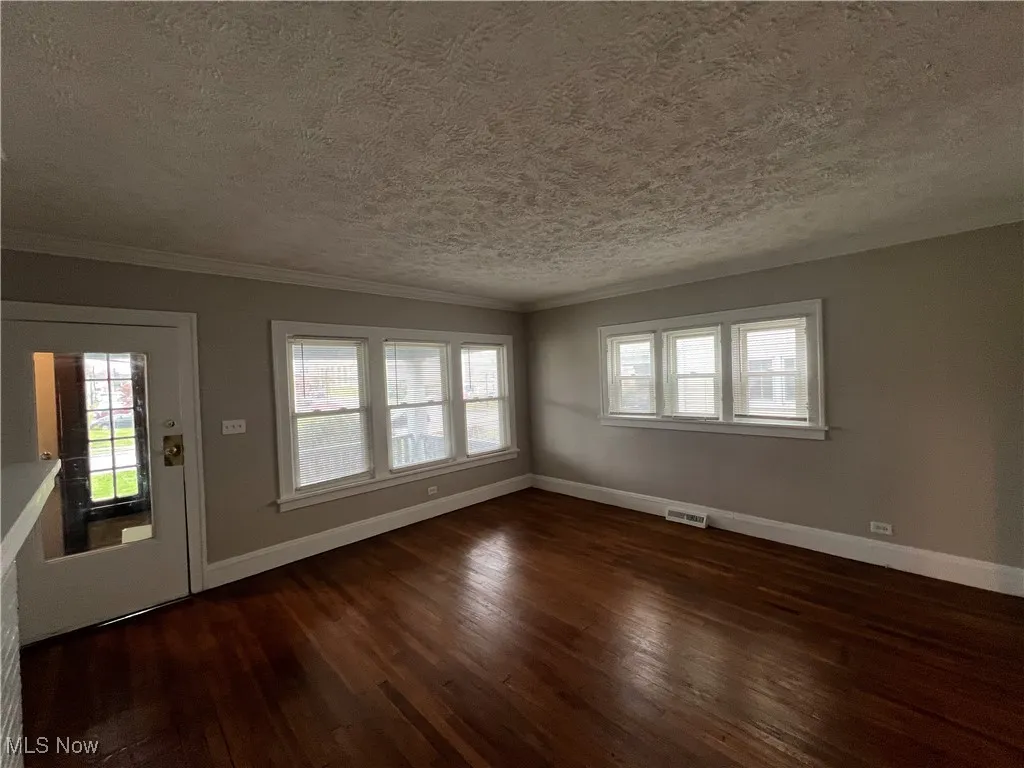 Unfurnished living room with hardwood / wood-style floors, a textured ceiling, and ornamental molding