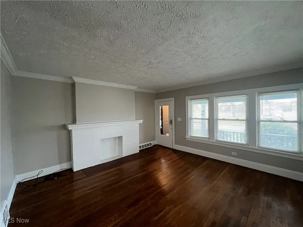 Unfurnished living room with dark wood finished floors, a textured ceiling, a fireplace, and crown molding