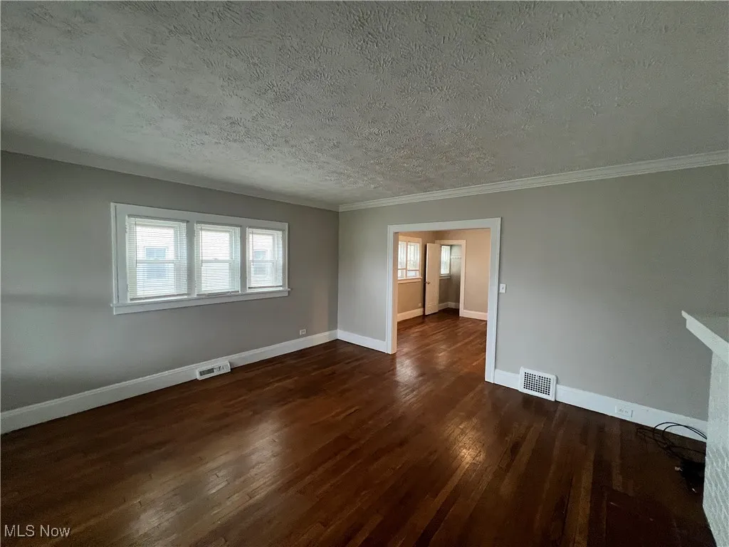 Unfurnished room with dark wood-style flooring, a textured ceiling, and crown molding