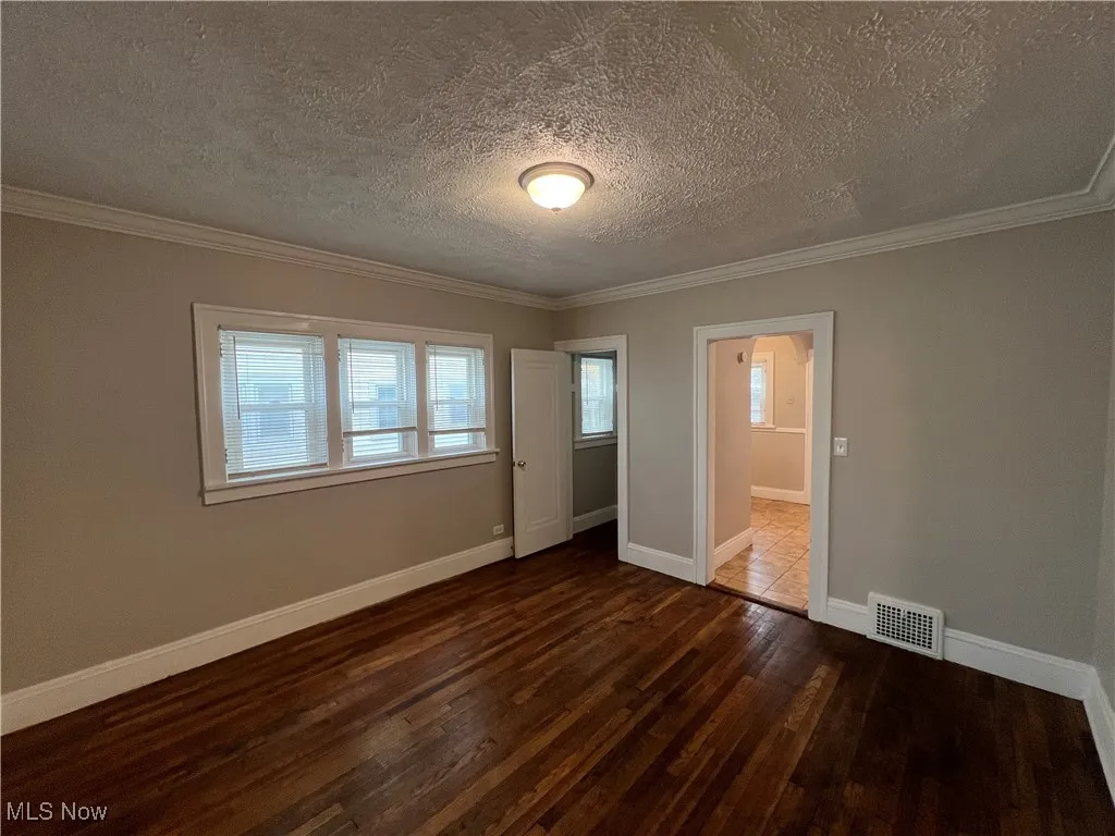 Unfurnished bedroom with dark wood-type flooring, a textured ceiling, and ornamental molding