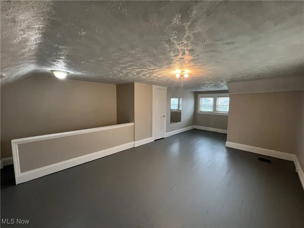 Spare room featuring a textured ceiling, dark wood-style flooring, and lofted ceiling