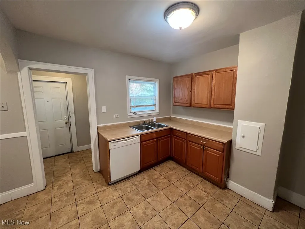 Kitchen featuring white dishwasher, light countertops, brown cabinetry, and light tile patterned floors