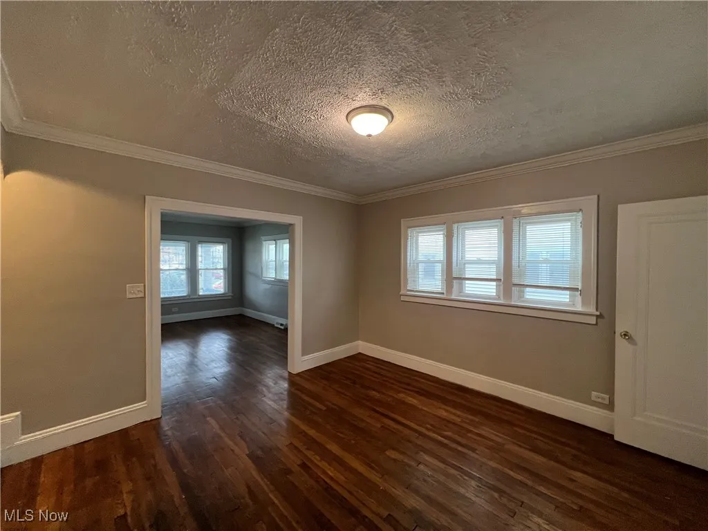 Empty room with dark wood-style flooring, a textured ceiling, and ornamental molding