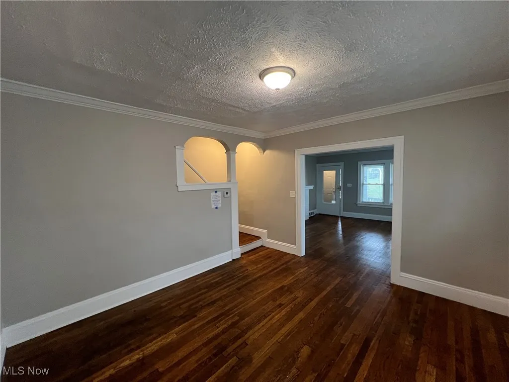 Unfurnished room with wood finished floors, a textured ceiling, crown molding, and arched walkways