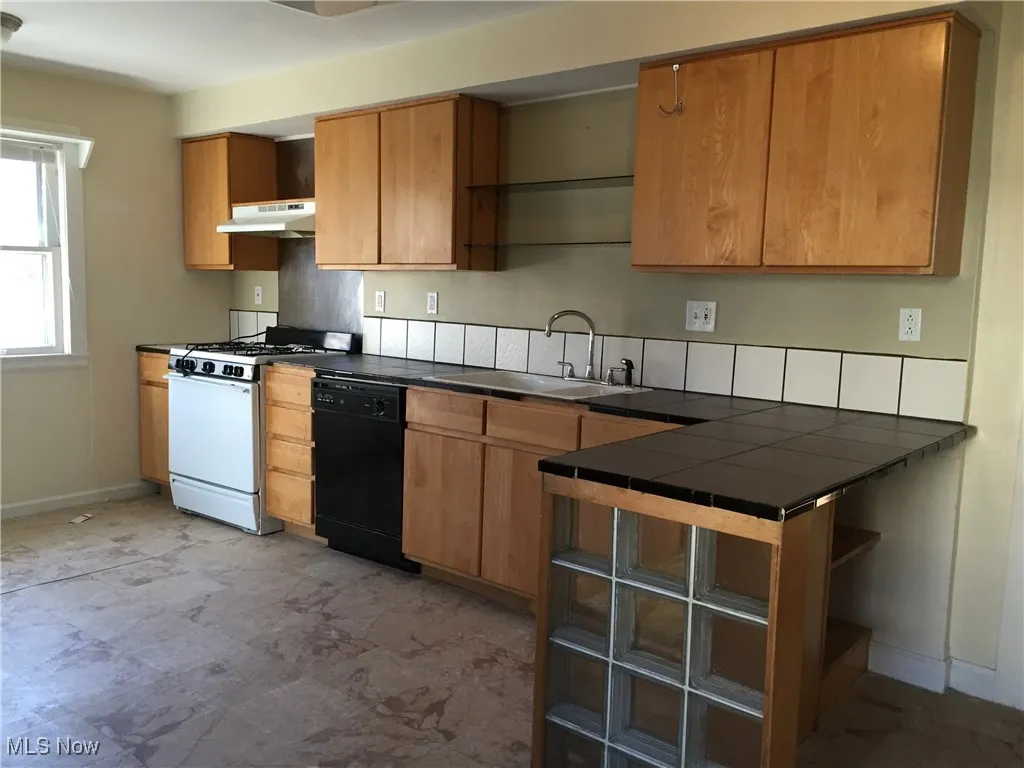 Kitchen with open shelves, black dishwasher, white gas stove, under cabinet range hood, and backsplash