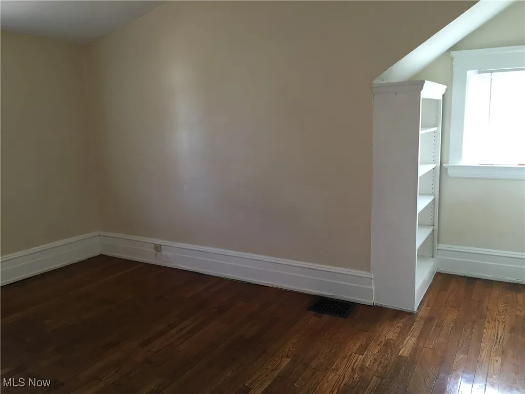 Spare room featuring dark wood-style flooring and baseboards