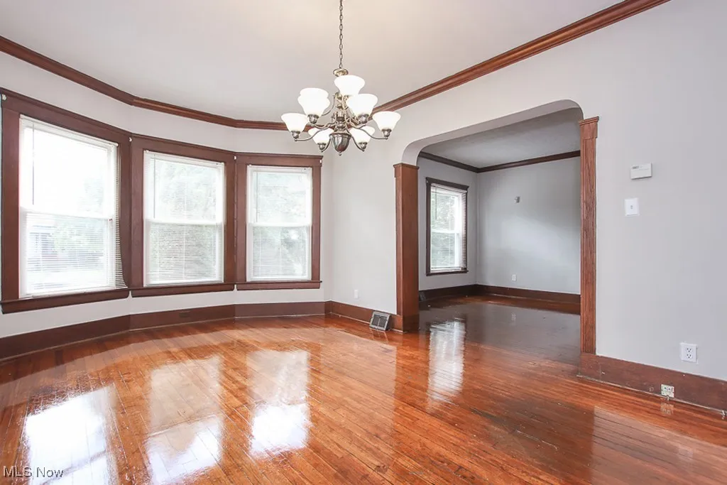 Unfurnished room featuring arched walkways, a chandelier, wood-type flooring, and crown molding