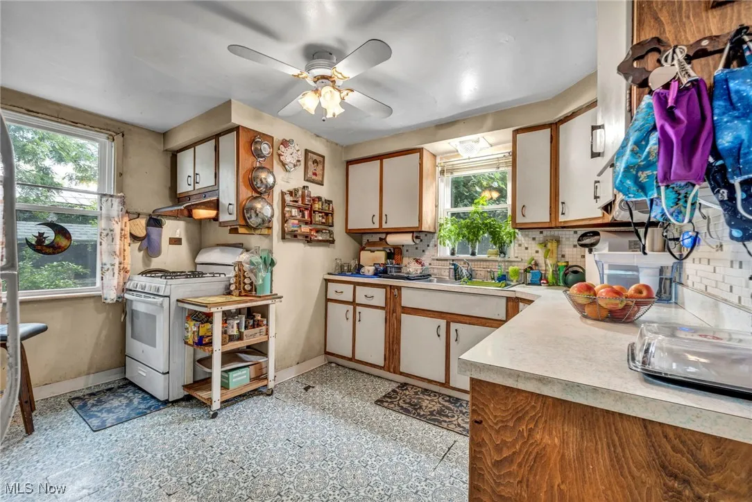 Kitchen featuring white gas range, light countertops, under cabinet range hood, ceiling fan, and decorative backsplash