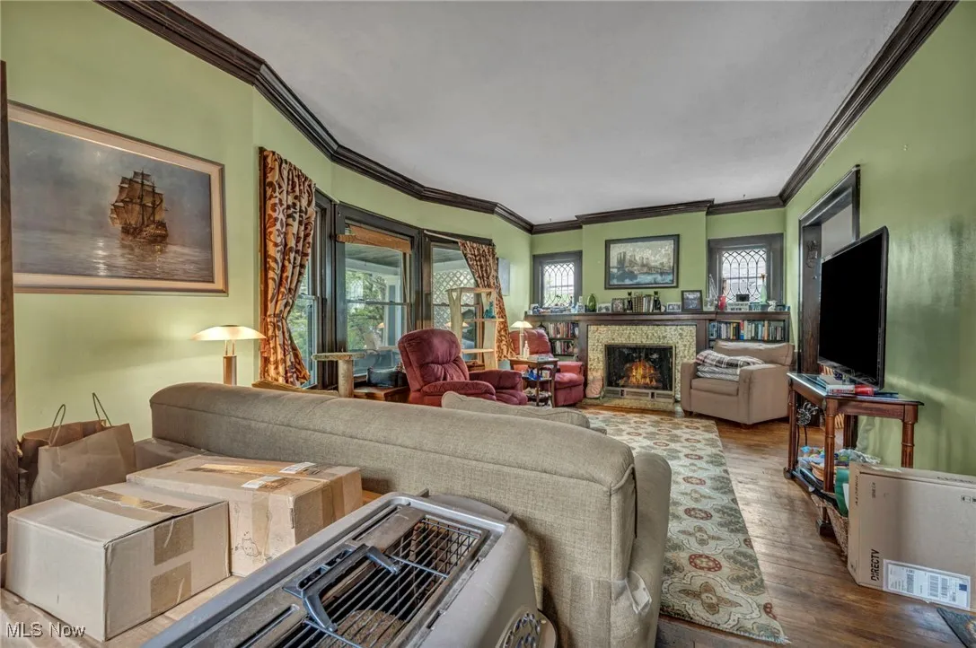 Living area with ornamental molding, wood finished floors, and a fireplace with flush hearth