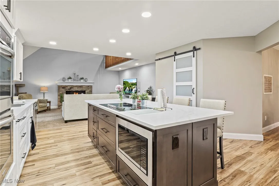 Kitchen with stainless steel microwave, light wood-type flooring, an island with sink, white cabinetry, and a barn door