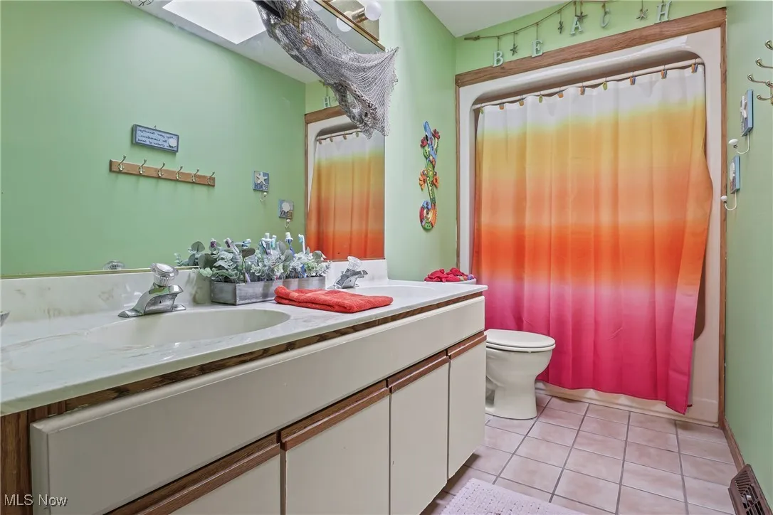 Bathroom featuring double vanity, tile patterned floors, curtained shower, and a skylight
