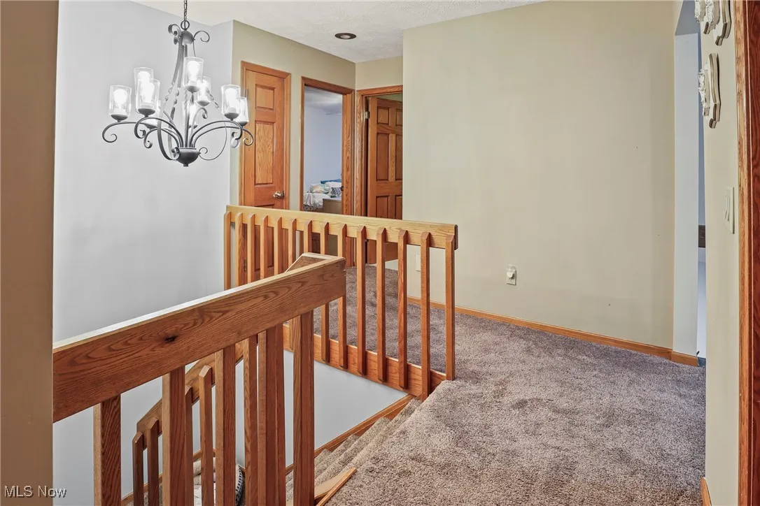 Hall featuring an upstairs landing, carpet, and a chandelier