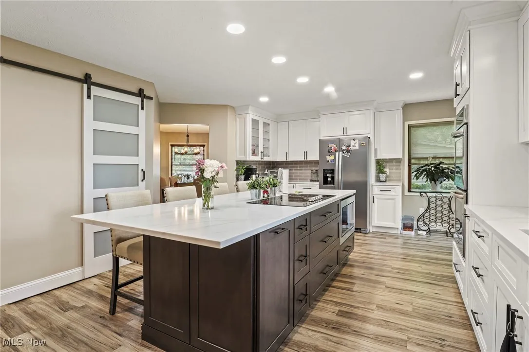 Kitchen with stainless steel appliances, white cabinets, light wood-style floors, a kitchen island, and a kitchen bar