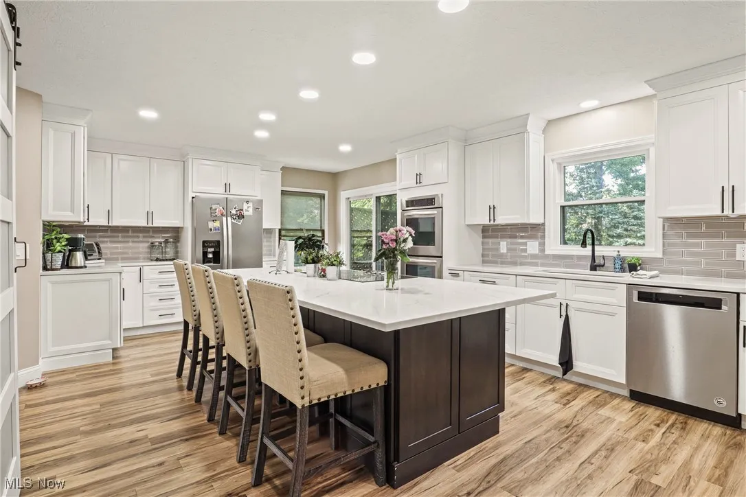 Kitchen with appliances with stainless steel finishes, tasteful backsplash, light wood finished floors, a breakfast bar area, and white cabinetry
